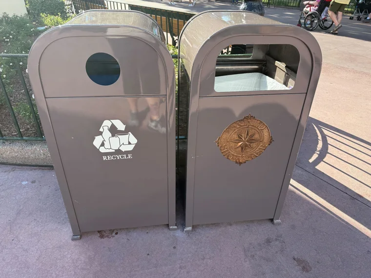Dos papeleras grises del World Showcase de Epcot, una de ellas con el emblema dorado en el frontal.