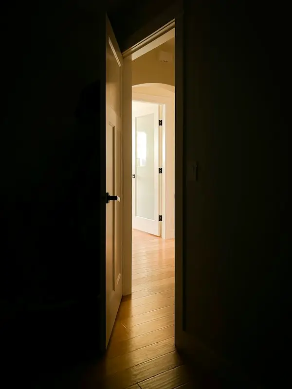 Una puerta entreabierta en una habitación a oscuras. Al otro lado, un pasillo iluminado.
